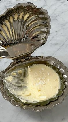 a silver bowl filled with cream sitting on top of a white marble counter next to a metal spoon