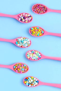 six pink spoons filled with sprinkles and candies on blue background