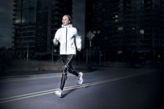 a man in white jacket and black pants running on street at night with buildings behind him