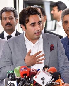 two men sitting at a table with microphones in front of them and one man holding his hand out