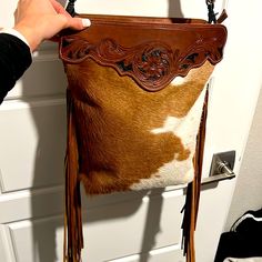 a cowhide purse being held up by a woman's hand in front of a door