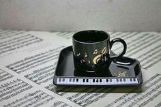 a black coffee cup sitting on top of a piano keyboard coaster next to sheet music