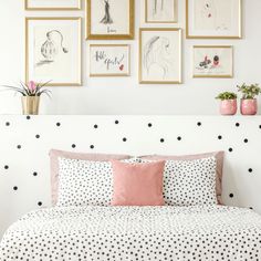 a white bed with black and white polka dot sheets, pink pillows and pictures on the wall above it