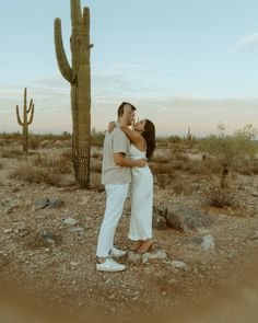 a man and woman kissing in front of a cactus