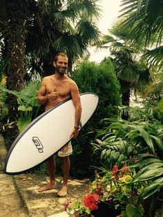 a shirtless man holding a surfboard in front of some tropical plants and trees