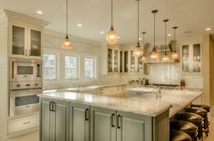 a large kitchen with lots of counter space and lights hanging from the ceiling over the island