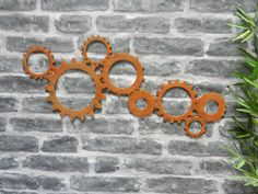 three orange gears on a brick wall next to a potted plant with green leaves