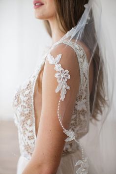 a woman in a wedding dress wearing a veil with flowers on the back of her shoulder