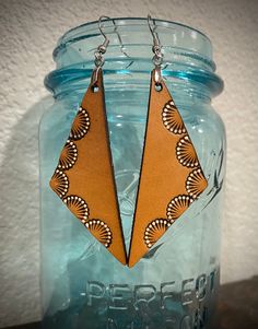 a pair of brown leather earrings sitting on top of a blue mason jar next to a white wall