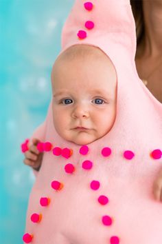 a woman holding a baby wearing a pink costume with pom poms on it's head