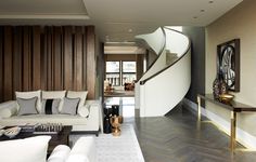 a living room filled with white couches and wooden paneled walls next to a spiral staircase