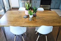 a wooden table with white chairs and plants on it in the middle of a kitchen