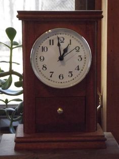 a small wooden clock sitting on top of a table next to a potted plant