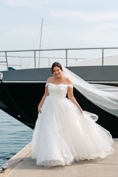 a woman in a white wedding dress standing on a dock next to a black boat