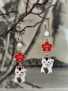 a pair of red and white cat earrings hanging from a tree branch