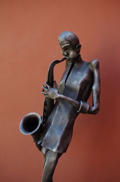 a statue of a woman playing the saxophone against a red wall with an orange background