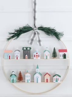 a christmas ornament is hanging on the wall with small houses and fir branches