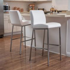 two white bar stools sitting on top of a hard wood floor in a kitchen