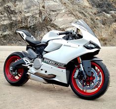 a white and red motorcycle parked in front of a rocky mountain side with mountains behind it