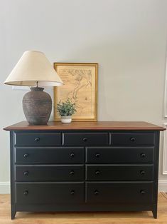 a black dresser with a lamp on top of it