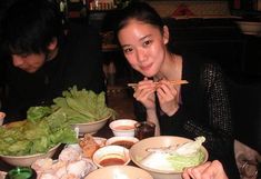 a woman sitting at a table eating food with chopsticks