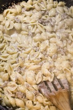 a skillet filled with macaroni and cheese being stirred by a wooden spoon