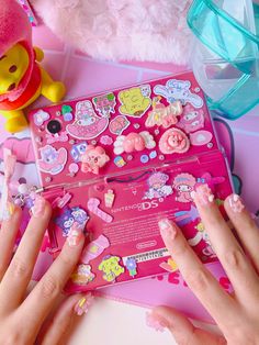 two hands with pink nail polish on their nails next to a box of stickers