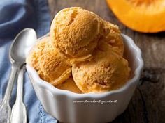 a white bowl filled with ice cream next to a spoon and orange slice on the table