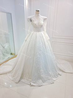 a white wedding dress on display in front of a mirror with an open back and long sleeves