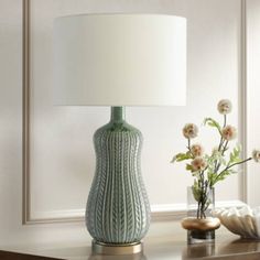 a green lamp sitting on top of a table next to a vase with flowers