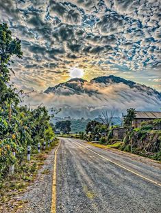 an empty road with mountains in the background and clouds above it at sunset or sunrise