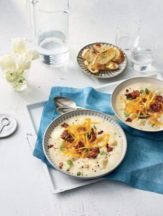 two bowls of soup with cheese and bacon in them on a blue napkin next to silverware