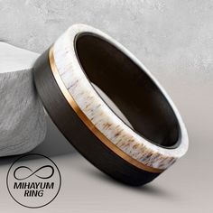 an unusual wooden ring with white and gold inlays sits next to a rock