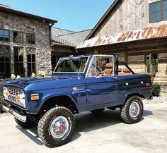 an old blue pickup truck parked in front of a large building with windows and doors