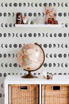 a small globe sits on top of a white cabinet in front of a black and white wallpaper