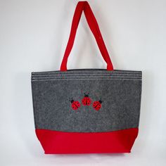 A sturdy red and grey colorblock felt tote with riveted web handles and three red and black Ladybugs embroidered on the front and back of the tote. Made out of 100% polyester felt and is approximately 12 inches tall by 12 inches wide by 4.5 inches deep. Wipe clean with a damp cloth. A fun tote to carry almost anything. Embroidered in the USA!  This item can be personalized with custom embroidery underneath the Ladybugs on the front and back of the tote. Embroidered School Tote Canvas Bag, Ladybug Felt, Embroidered Canvas Bag, Black Ladybug, Felt Tote, Beach Shopping, Embroidered Canvas, Lady Bugs, Personalized Embroidered