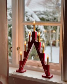 a candle holder in the shape of a triangle on a window sill with lit candles