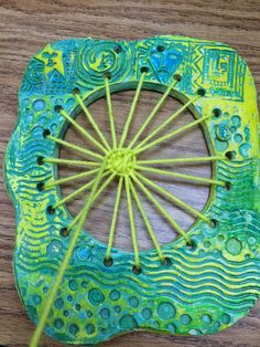 a close up of a green and yellow object on a wooden table with yarn in the middle