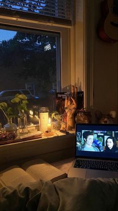 a laptop computer sitting on top of a window sill next to a plant and candles