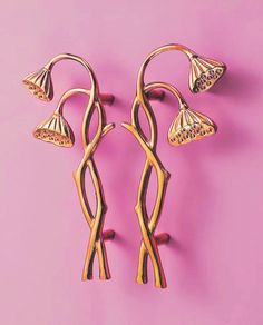 two gold earrings with flowers on them against a pink background in the style of art nouveauism