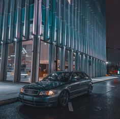 a car parked in front of a tall building on a wet street at night time