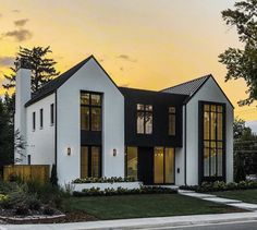 a white house with black trim and windows on the front, along side a street at sunset