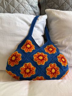 a crocheted bag sitting on top of a bed next to pillows and blankets