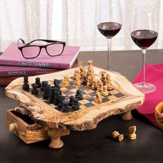 a wooden chess board with two glasses on it and some books next to it in front of them