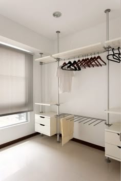 an empty room with clothes hanging on rails and drawers in the corner, next to a window