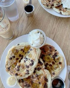 pancakes with bananas, raisins and whipped cream are on a white plate next to two glasses of water