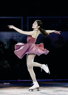 a woman in a pink dress skating on an ice rink with her arms out and one leg extended