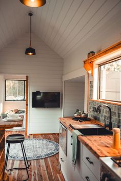 a kitchen with wooden floors and white walls, has a tv mounted on the wall