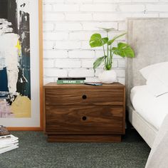 a bedroom with a bed, nightstand and painting on the wall behind it in front of a white brick wall