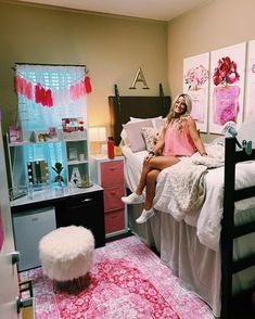 a woman sitting on top of a bed in a room with pink and white decor